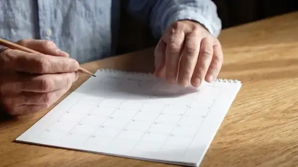 A pencil circling a date about a month ahead on a plain paper calendar lying on a kitchen table